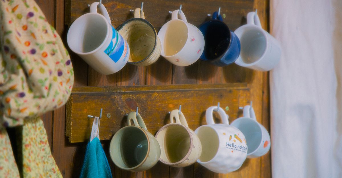 Rustic wooden rack with ceramic mugs hanging neatly, evoking cozy kitchen vibes.